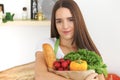 Young caucasian woman in a green apron is holding paper bag full of vegetables and fruits while smiling in kitchen Royalty Free Stock Photo