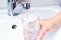 Young caucasian woman hand holding a glass with pure drinking water pouring from home faucet close up. Royalty Free Stock Photo