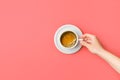 Young caucasian woman hands holds white cup with freshly brewed coffee with crema on saucer on pink background. Morning breakfast