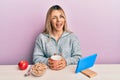 Young caucasian woman having breakfast looking at the tablet sitting on the tablet winking looking at the camera with sexy