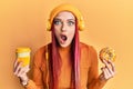 Young caucasian woman having breakfast using headphones afraid and shocked with surprise and amazed expression, fear and excited Royalty Free Stock Photo