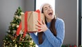 Young caucasian woman hearing sound of christmas gift at home