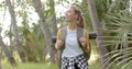 Young Caucasian woman hikes through a lush park, looking around with a smile