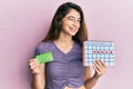 Young caucasian woman holding birth control pills and menstrual calendar winking looking at the camera with sexy expression, Royalty Free Stock Photo