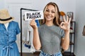 Young caucasian woman holding black friday banner at retail shop doing ok sign with fingers, smiling friendly gesturing excellent Royalty Free Stock Photo