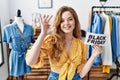 Young caucasian woman holding black friday banner at retail shop doing ok sign with fingers, smiling friendly gesturing excellent Royalty Free Stock Photo