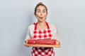 Young caucasian woman holding board with raw meat making fish face with mouth and squinting eyes, crazy and comical Royalty Free Stock Photo