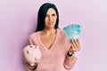 Young caucasian woman holding brazil real banknotes and piggy bank clueless and confused expression Royalty Free Stock Photo