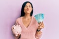 Young caucasian woman holding brazil real banknotes and piggy bank looking at the camera blowing a kiss being lovely and sexy