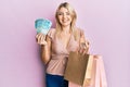 Young caucasian woman holding brazil real banknotes and shopping bags winking looking at the camera with sexy expression, cheerful