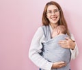 Young caucasian woman holding and carrying baby on a sling looking positive and happy standing and smiling with a confident smile Royalty Free Stock Photo