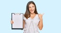 Young caucasian woman holding clipboard with blank space pointing thumb up to the side smiling happy with open mouth Royalty Free Stock Photo