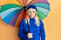 Young caucasian woman holding colorful umbrella making fish face with mouth and squinting eyes, crazy and comical