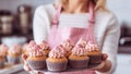 Young caucasian woman holding cupcakes in the kitchen. Cakes cupcakes and sweet dessert pink girly concept. holding her