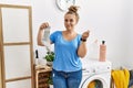 Young caucasian woman holding dirty sock at laundry room doing money gesture with hands, asking for salary payment, millionaire Royalty Free Stock Photo