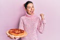 Young caucasian woman holding italian pizza pointing thumb up to the side smiling happy with open mouth Royalty Free Stock Photo