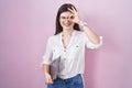 Young caucasian woman holding laptop doing ok gesture with hand smiling, eye looking through fingers with happy face Royalty Free Stock Photo