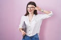 Young caucasian woman holding laptop doing peace symbol with fingers over face, smiling cheerful showing victory Royalty Free Stock Photo