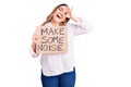 Young caucasian woman holding make some noise banner smiling happy doing ok sign with hand on eye looking through fingers Royalty Free Stock Photo