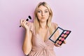 Young caucasian woman holding makeup brush and blush palette puffing cheeks with funny face