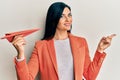 Young caucasian woman holding paper airplane smiling happy pointing with hand and finger to the side Royalty Free Stock Photo