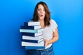 Young caucasian woman holding a pile of books afraid and shocked with surprise and amazed expression, fear and excited face Royalty Free Stock Photo