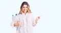 Young caucasian woman holding recycling plastic bottles smiling happy pointing with hand and finger to the side Royalty Free Stock Photo