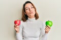 Young caucasian woman holding red and green apple looking at the camera blowing a kiss being lovely and sexy Royalty Free Stock Photo