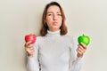 Young caucasian woman holding red and green apple puffing cheeks with funny face Royalty Free Stock Photo