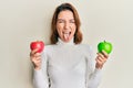 Young caucasian woman holding red and green apple sticking tongue out happy with funny expression Royalty Free Stock Photo