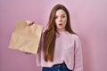 Young caucasian woman holding shopping bag and credit card scared and amazed with open mouth for surprise, disbelief face Royalty Free Stock Photo