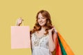 Young caucasian woman holding shopping bags while standing on a yellow background with copy space Royalty Free Stock Photo