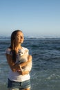 Young Caucasian woman holding small white chihuahua dog and enjoying sunset at the beach. Closed eyes. Relaxed and peaceful mood.