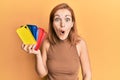 Young caucasian woman holding smartphone case scared and amazed with open mouth for surprise, disbelief face Royalty Free Stock Photo