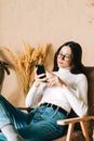 Young caucasian woman holding smartphone looking on cell using mobile phone technology at home sitting on armchair Royalty Free Stock Photo