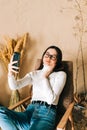 Young caucasian woman holding smartphone looking on cell using mobile phone technology at home taking selfie for social media or Royalty Free Stock Photo