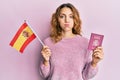 Young caucasian woman holding spain flag and passport puffing cheeks with funny face