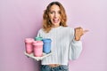 Young caucasian woman holding tray with take away coffee pointing thumb up to the side smiling happy with open mouth Royalty Free Stock Photo