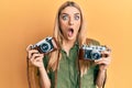 Young caucasian woman holding vintage camera afraid and shocked with surprise and amazed expression, fear and excited face Royalty Free Stock Photo