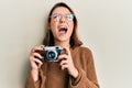 Young caucasian woman holding vintage camera angry and mad screaming frustrated and furious, shouting with anger looking up Royalty Free Stock Photo