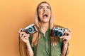 Young caucasian woman holding vintage camera angry and mad screaming frustrated and furious, shouting with anger looking up Royalty Free Stock Photo