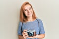 Young caucasian woman holding vintage camera looking positive and happy standing and smiling with a confident smile showing teeth Royalty Free Stock Photo