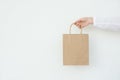 Young caucasian woman holds in hand empty blank mock up brown craft paper bag on white wall background. Christmas New Years
