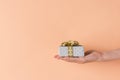 Young Caucasian woman holds in hand gift box wrapped in silver paper with golden ribbon bow on ink background. Christmas New Years