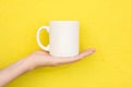 Young Caucasian Woman Holds on Hand Palm Blank Mockup White Mug on Bright Yellow Painted Wall. Airy Breezy Style