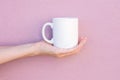 Young Caucasian Woman Holds on Hand Palm Blank Mockup White Mug on Light Pink Painted Wall. Airy Breezy Style