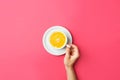 Young caucasian woman holds with hand white coffee cup with fresh halved orange in middle on pink background. Funky creative food Royalty Free Stock Photo