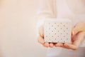 Young caucasian woman holds in hands small gift box wrapped in grey paper with polka dot pattern. White background pastel colors