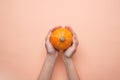 Young Caucasian Woman Holds in Hands Small Round Heirloom Orange Pumpkin on Peachy Pink Background. Fall Autumn