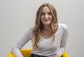 Young caucasian woman interested in coversation and looking at camera while sitting in chair, grey background